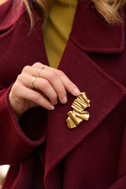 Kate Gold sculptural magnetic brooch worn on a burgundy coat; the full folded gold shape is clearly visible.