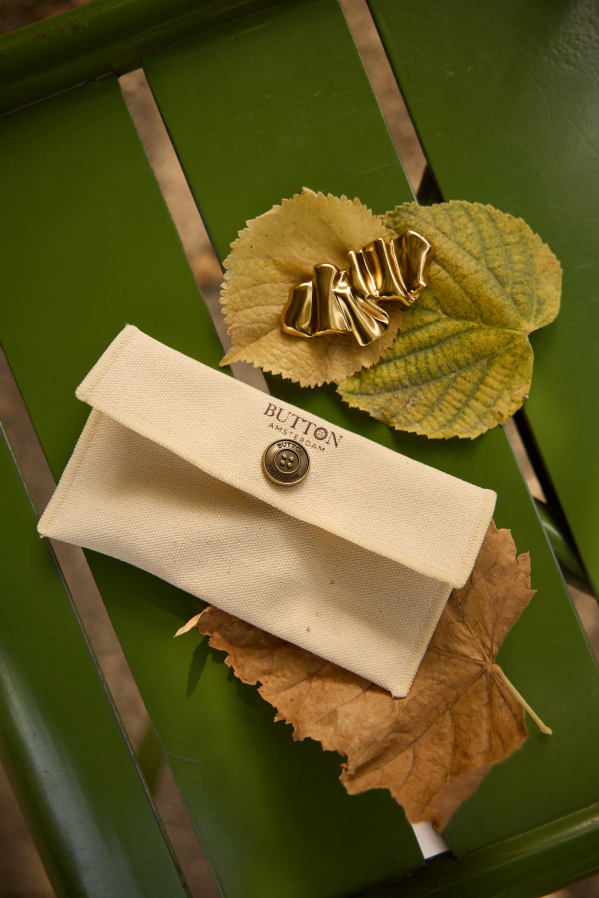 Kate Gold sculptural magnetic brooch displayed on an autumn leaf beside a Button Amsterdam fabric pouch.