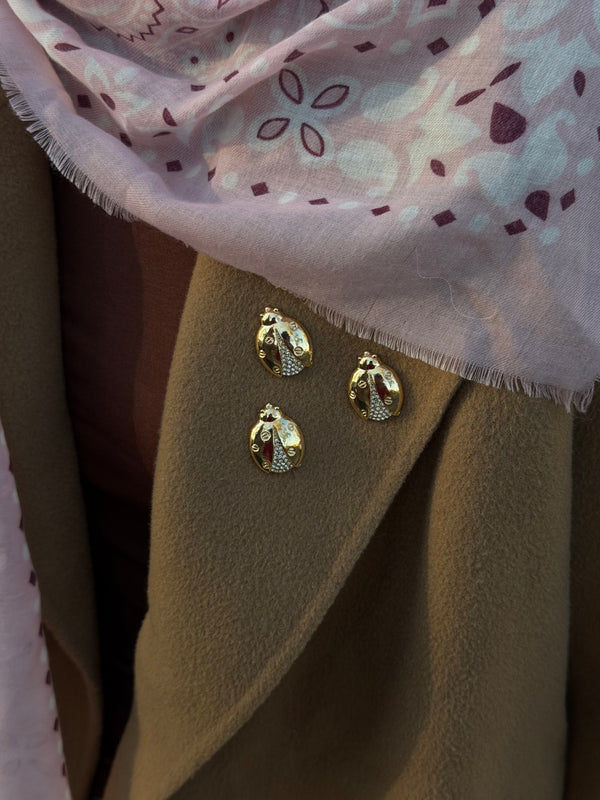 Three ladybird magnetic brooches styled on a camel coat lapel with a pink scarf.