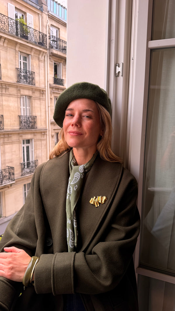 Sculptural gold magnetic brooch styled on an olive blazer by a balcony.